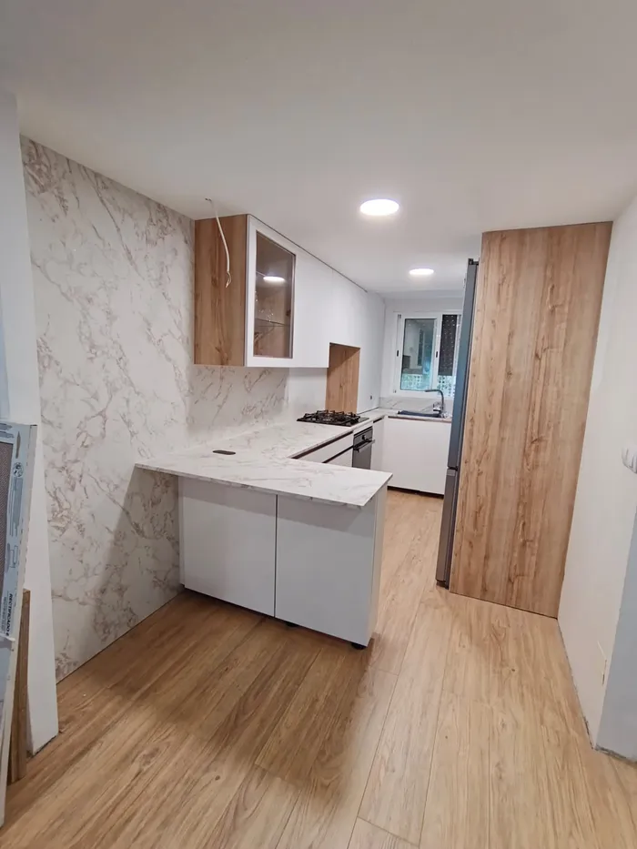 Cocina blanca con encimera de mármol y frontal de madera montada en Hospitalet de Llobregat