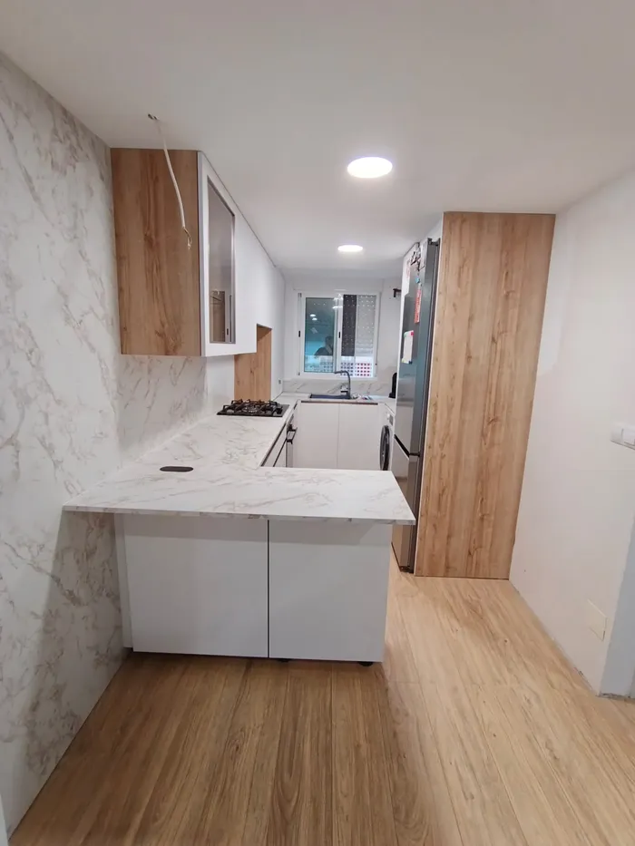 Detalle de cocina en L con muebles blancos y encimera de mármol